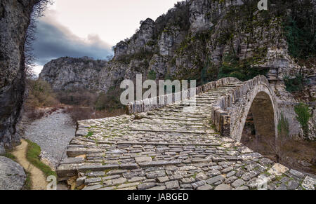 Alte Kokkori - Noutsou gewölbten Steinbrücke über die Vikos-schlucht, Zagorochoria, Griechenland. Winter Sonnenuntergang mit Eis und Gletscher auf dem Fluss. Stockfoto