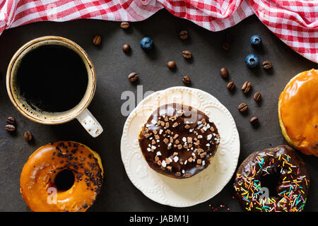 Leckere Donuts Schoko Karamell Zuckerglasur und Tasse schwarzen Kaffee Espresso auf Tisch. Ansicht von oben Stockfoto