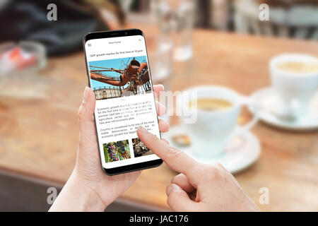 News-Artikel mit Ihrem Smartphone zu lesen. News Portal-Website mit Unternehmensinformationen. Wirtschaftswachstum-Artikel. Kaffee am Tisch im Hintergrund. Stockfoto