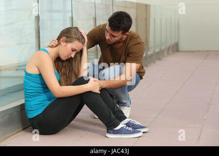Schöne Teenager-Mädchen sitzen auf dem Boden und ein Junge tröstlich ihr besorgt Stockfoto