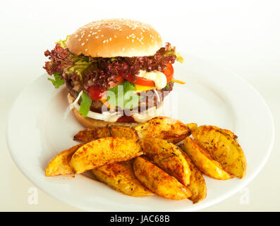 Cheeseburger mit Kartoffelspalten auf Teller; grün-weiß gestreifte Tischdecke, Tomaten als Dekoration Stockfoto