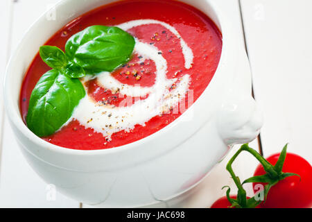 Nahaufnahme der geneigten Winkel einer Schüssel bunten roten frische Tomatensuppe mit Sahne beträufelt und mit Basilikum garniert Stockfoto