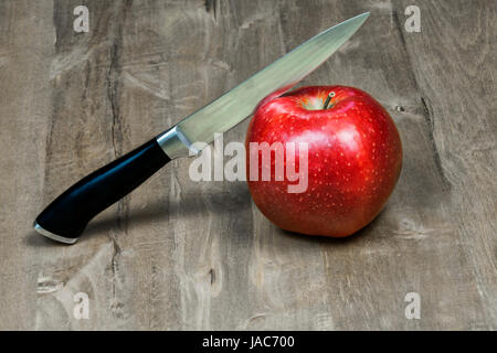 Das Messer schneidet einen roten Apfel auf einer Holzfläche liegend Stockfoto