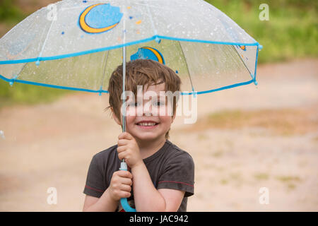 Lächelnde junge hält ein Dach unter dem Regen Stockfoto