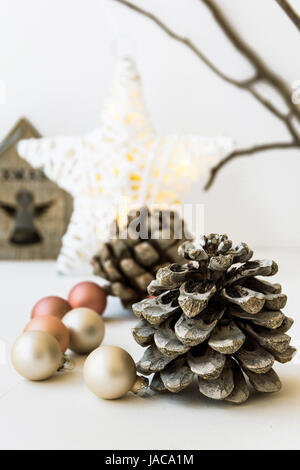 White Christmas-Dekoration-Zusammensetzung, großer Tannenzapfen, verstreuten Kugeln, glänzenden Stern, hölzerne Kerzenständer, trockene Äste im Hintergrund, Nahaufnahme Stockfoto