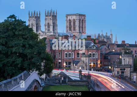 Stadtmauer, Straße über Lendal Bridge & 3 dunklen Abendhimmel, ikonischen Türme des Münsters gegenübergestellt Leuchten von Straßenlaternen & Lichtspuren - York, GB, UK. Stockfoto