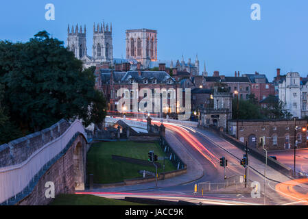 Stadtmauer, Straße über Lendal Bridge & 3 dunklen Abendhimmel, ikonischen Türme des Münsters gegenübergestellt Leuchten von Straßenlaternen & Lichtspuren - York, GB, UK. Stockfoto