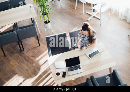 Draufsicht der Weibchen mit ihrem Laptop in einem Café. Overhead Schuss von junge Frau sitzt an einem Tisch mit einer Tasse Kaffee und Handy-Surfen im Netz auf ihrem Laptop-Computer. Stockfoto