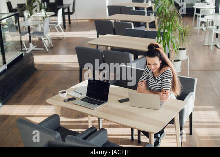 Draufsicht der jungen Frau, die Überprüfung Zeit auf ihrer Smartwatch während der Arbeit an ihrem Laptop in einem Café. Ansicht von oben geschossen Frau sitzt an einem Tisch mit einer Tasse Kaffee, Laptop und Handy. Stockfoto