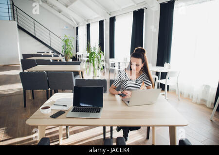 Attraktive Frau zu ihrer Arbeit hält Telefon und sitzen mit einem Laptop. Schönen weiblichen Multitasking. Stockfoto