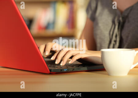 Nahaufnahme von Mädchen Hände schreiben in einem roten Laptop auf dem Tisch zu Hause ein warmes Licht und einen bunten Hintergrund Stockfoto