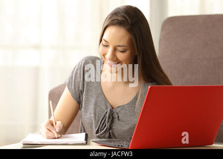 Schüler lernen und Notizen in einem Notizbuch aus Papier mit einem roten Laptop neben sitzen auf dem Boden im Wohnzimmer zu Hause Stockfoto