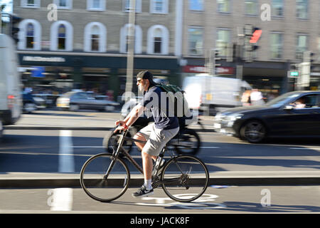 Junger Mann in kurzen Hosen und Baseball-Cap, Radfahren durch Kings Cross, London, in der Rush hour Stockfoto