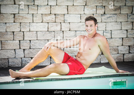 Schöner junger Mann liegt mit Shorts am Rande eines Swimmingpools Stockfoto