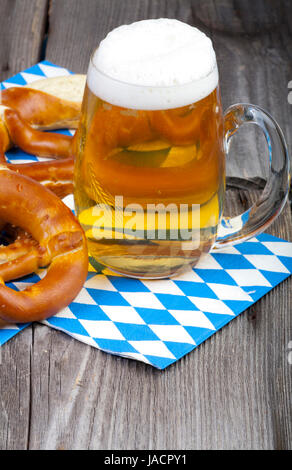 Ein Großes Kühles Bier Und Brezeln Auf Servietten Mit Blau-Weißen Rautenmuster Auf Einem alten Rustikalem Holztisch Stockfoto