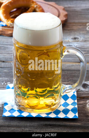 Großen Kühles Glas Bier Auf Einer Serviette Mit Blau-Weißem Rautenmuster Auf Einem alten Rustikalem Holztisch Im Hintergrund Ein Holzbrett Mit Brezeln Stockfoto