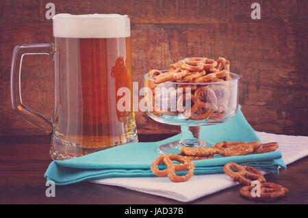 Glas Bier in Stein mit Mini Brezeln auf blass blauen Serviette auf Holz Hintergrund mit angewandter Retro-Stil-Filter. Stockfoto