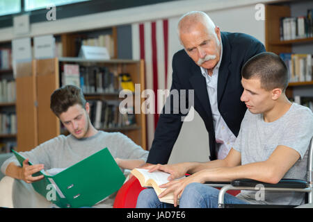 Lehrer-Schüler im Rollstuhl mit einem Mitschüler in der Bibliothek arbeiten Stockfoto