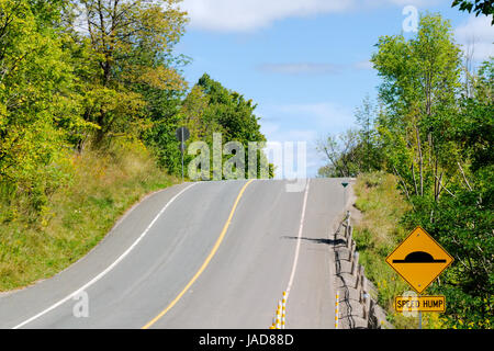 Hügel auf Landstraße mit gelben Bremsschwelle Warnschild. Stockfoto