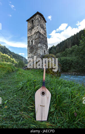 Georgische nationale Musikinstrument der Panduri mit einem mittelalterlichen Turm im Hintergrund, in der Region Swanetien von den Bergen des Kaukasus in Georgien. Stockfoto