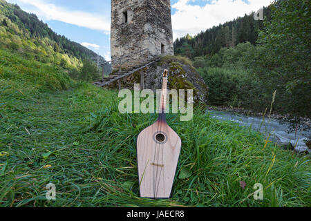 Georgische nationale Musikinstrument der Panduri mit einem mittelalterlichen Turm im Hintergrund, in der Region Swanetien von den Bergen des Kaukasus in Georgien. Stockfoto