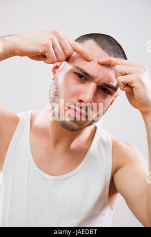 Junger Mann drückt Pickel auf der Stirn. Stockfoto