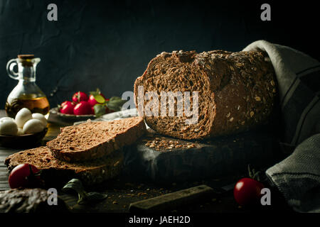 Vollkornbrot auf Holzbrett mit Olivenöl, Tomaten und Basilikum. Dunkel getönten Foto mit Textfreiraum. Stockfoto