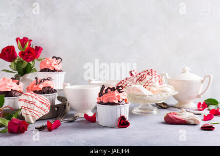 Schöne Schokolade Cupcake, rosa Sahne, Baiser Cookies und rote Rosen auf grauem Stein Hintergrund. Valentinstag, Muttertag, Hochzeitskonzept mit Co Stockfoto