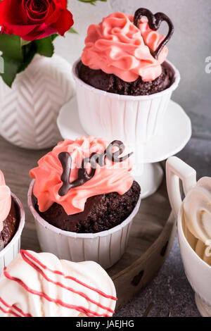Schöne Schokolade Cupcake, rosa Sahne, Baiser Cookies und rote Rosen auf grauem Stein Hintergrund. Valentinstag, Muttertag, Hochzeitskonzept. Stockfoto