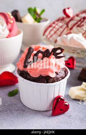 Schöne Schokolade Cupcake, rosa Sahne, Baiser Cookies und rote Rosen auf grauem Stein Hintergrund. Valentinstag, Muttertag, Hochzeitskonzept. Stockfoto