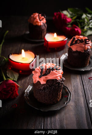 Schöne Schokolade Cupcake mit rosa Creme auf hölzernen Hintergrund. Valentinstag, Muttertag, Hochzeit Grußkarte. Dunkles Foto. Stockfoto