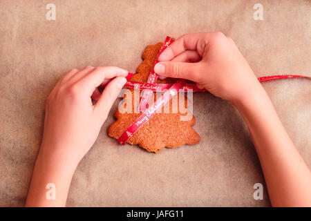 Weibliche Hände binden gebackenen Lebkuchen Weihnachtsplätzchen mit Band Stockfoto