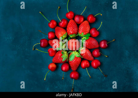 Reife Bio-Erdbeeren, glänzend Süßkirschen angeordnet in Form von Blumen, blauer Hintergrund, Stil, kreative Bild, gesunde Ernährung, Plakat Vorlage f Stockfoto