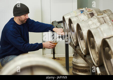 Menschen zeichnen einige Bier aus einem Metall Fass in einer Brauerei zum testen. Stockfoto