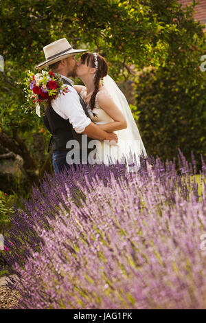 Brautpaar stehend im Freien in einem Garten, umarmen und küssen. Stockfoto