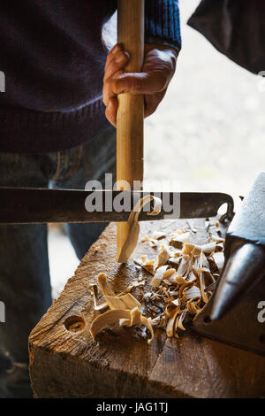 Ein Mann in einem Workshop halten eines Werkzeugs schneiden und Formen ein Stück Holz. Stockfoto