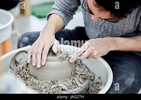 Ein Mann sitzt auf einer Töpferscheibe arbeiten und gestalten einen Tontopf durch Entfernen der überschüssigen Ton. Stockfoto