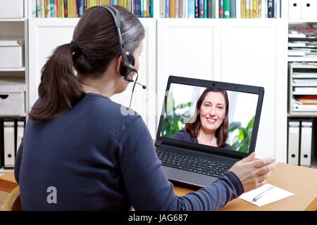 Frau mit Kopfhörer an ihrem Schreibtisch vor Ihrem Laptop eine oline Telefonat mit ihr glücklicher Freund, text Raum Stockfoto