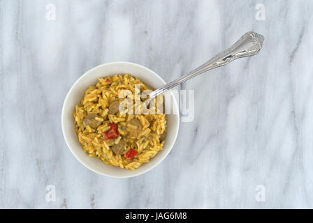 Draufsicht der Korma Curry-Sauce mit Pilau Reis in eine Schüssel auf einem Marmortisch Top weiß mit einer Gabel in das Essen gemischt. Stockfoto