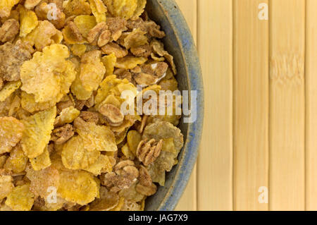 Enge Draufsicht eine alte Steingut-Schale mit trockenen Mehrkorn Frühstücks-Cerealien auf Holz Tischset gefüllt. Stockfoto