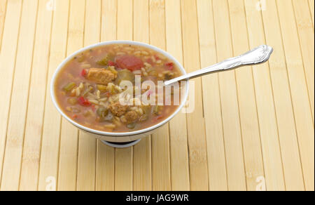 Eine Schüssel mit Gumbo mit Fleisch, Reis und Gemüse in einer Brühe mit einem Löffel in das Essen auf einem Holz-Platz-Matte. Stockfoto