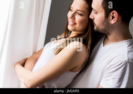 Junger Kerl umarmt seine Freundin und beide Blick durch Fenster Stockfoto