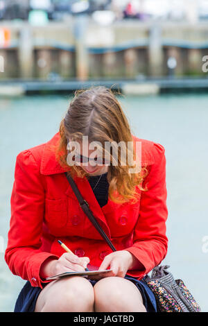 Frau, die im Juni in Weymouth, Dorset UK, am Hafen Postkarten schreibt Stockfoto