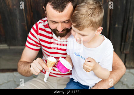 Junger Vater und seinen kleinen Sohn Eis essen. Sonniger Tag. Stockfoto