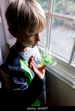 Ein Junge spielt mit einem Fidget Spinner zu Hause das umstrittene Stress Relief Spielzeug gefunden, einige kribbelig oder autistischen Kindern helfen Konzentrat in der Schule Stockfoto