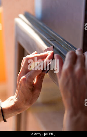 Hände einer Frau mit Sandpapier tun DIY arbeiten auf hölzernen Befestigungen Stockfoto