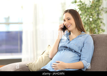 Schwangere Frau telefonieren mit dem Handy sitzt auf einer Couch im Wohnzimmer zu Hause Stockfoto