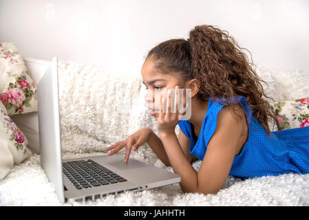 Ein junge schwarze Teenager-Mädchen auf der Couch zu legen und einen Laptop verwenden Stockfoto