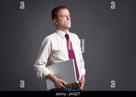 Ein Mann mittleren Alters mit einem Laptop stehen und blickte seitlich Stockfoto
