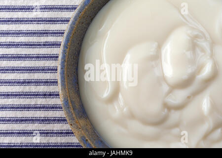 Enge Draufsicht eine alte Steingut-Schale gefüllt mit Vanille-Joghurt auf eine blau gestreifte Tischdecke. Stockfoto